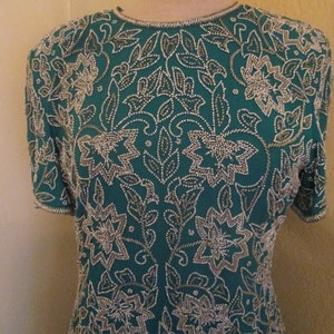 May include: A teal blue top with a silver floral pattern. The top is made of a soft, silky fabric and is fully beaded.