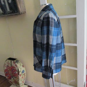 Puede incluir: Chaqueta a cuadros azul, negra y gris sobre un maniqu&iacute;. La chaqueta tiene un dise&ntilde;o cl&aacute;sico con botones, mangas largas y cuello. El patr&oacute;n de cuadros es una mezcla de tonos claros y oscuros.