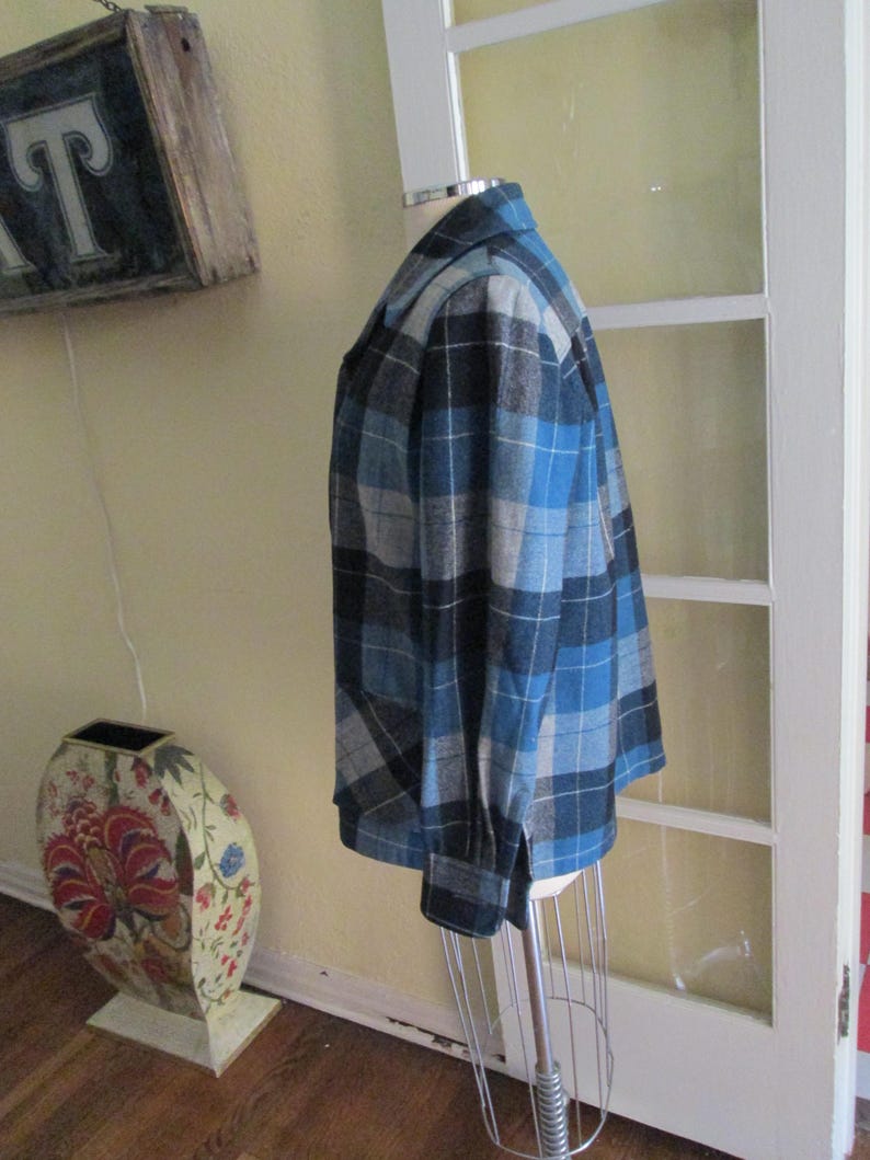 Puede incluir: Chaqueta a cuadros azul, negra y gris sobre un maniqu&iacute;. La chaqueta tiene un dise&ntilde;o cl&aacute;sico con botones, mangas largas y cuello. El patr&oacute;n de cuadros es una mezcla de tonos claros y oscuros.