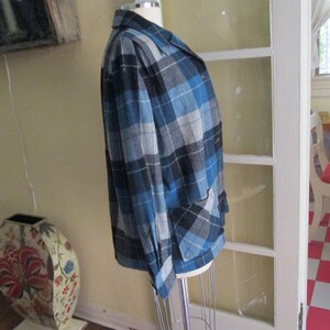 Puede incluir: Un blazer a cuadros azul, negro y gris sobre un maniqu&iacute;. La chaqueta tiene un cuello cl&aacute;sico, dos bolsillos delanteros y cierre de bot&oacute;n. El patr&oacute;n de cuadros es una mezcla de tonos claros y oscuros de azul, negro y gris.
