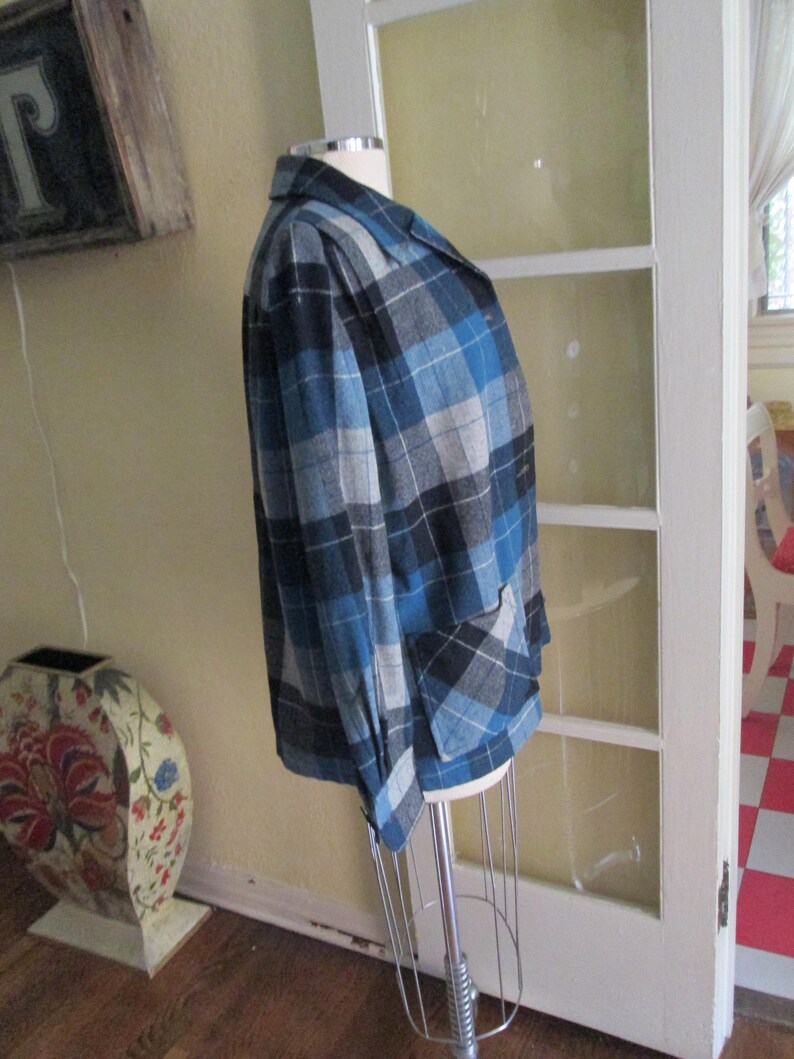 Puede incluir: Un blazer a cuadros azul, negro y gris sobre un maniqu&iacute;. La chaqueta tiene un cuello cl&aacute;sico, dos bolsillos delanteros y cierre de bot&oacute;n. El patr&oacute;n de cuadros es una mezcla de tonos claros y oscuros de azul, negro y gris.