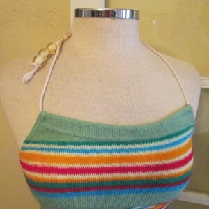 May include: A colorful halter top with horizontal stripes in shades of teal, orange, pink, blue, and white. The top is displayed on a mannequin and features a beaded strap and a tassel.