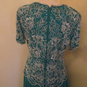 May include: A teal blue dress with a silver floral pattern. The dress has short sleeves and a fitted bodice.