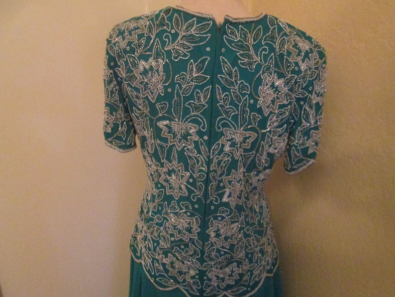 May include: A teal blue dress with a silver floral pattern. The dress has short sleeves and a fitted bodice.