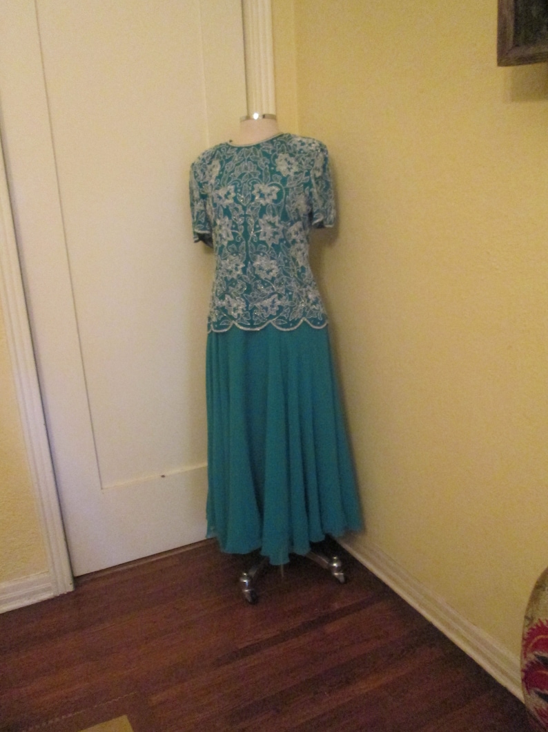 May include: A teal formal dress with a white lace bodice. The dress is on a mannequin and has a skirt that falls to the floor.