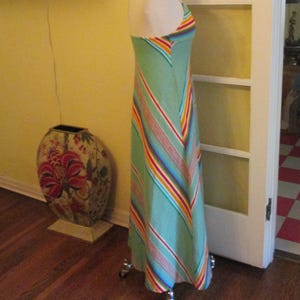 May include: A light green halter maxi dress with colorful diagonal stripes. The dress is displayed on a mannequin. The stripes include red, orange, yellow, and blue. The dress is floor length.