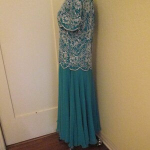 May include: A teal blue formal gown with a white beaded bodice and a flowing skirt. The gown is on a dress form.
