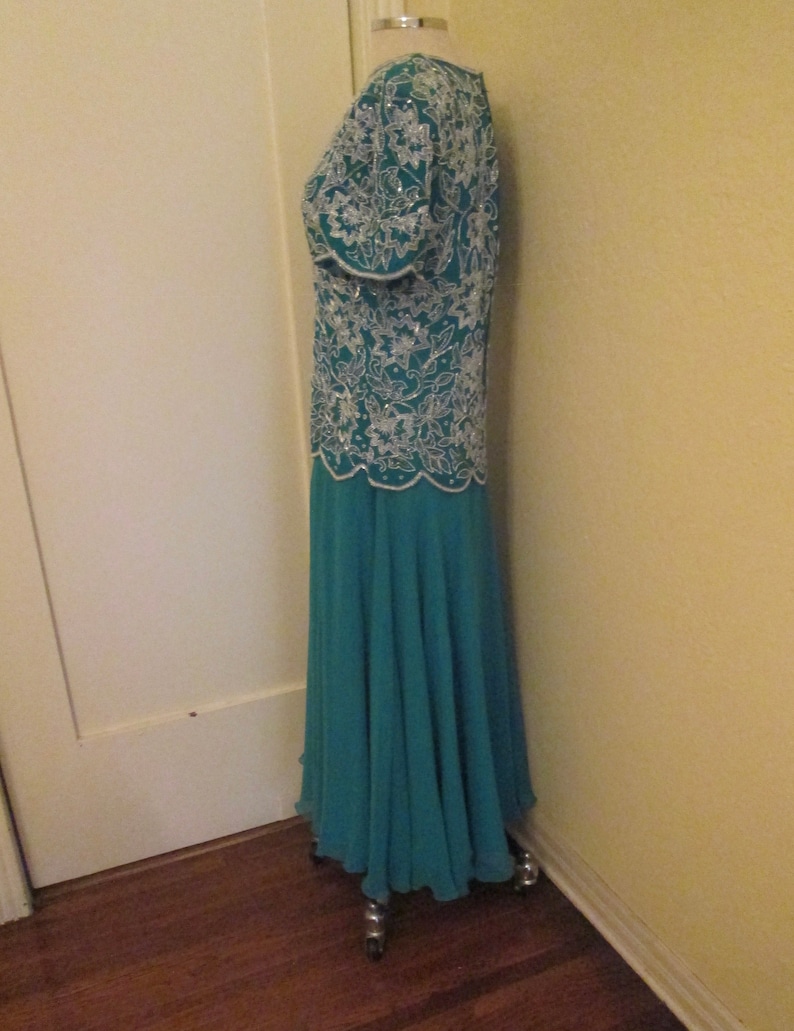 May include: A teal blue formal gown with a white beaded bodice and a flowing skirt. The gown is on a dress form.