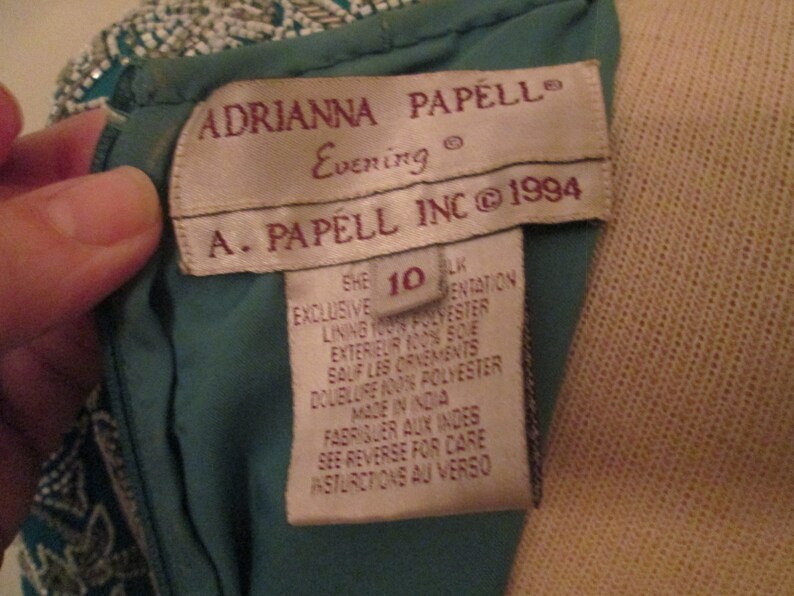 May include: A teal blue dress with a beaded bodice and a white tag that reads "ADRIANNA PAPELL Evening" and "A. PAPELL INC &copy; 1994". The tag also includes size and care instructions.