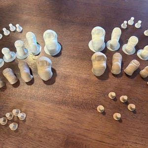 May include: An overhead shot displays an assortment of small, finger-shaped objects in varying shades of white and tan. Some have a flat base, while others are rounded. The objects are arranged on a dark wooden surface.