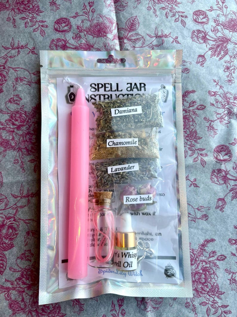 May include: A pink spell jar kit in a clear plastic bag. The kit includes a pink candle, small glass bottles, dried herbs labeled Damiana, Chamomile, and Lavender, and a bottle of spell oil. The text "Spell Jar Instructions" is visible.