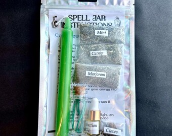 May include: A spell jar kit in a clear, iridescent pouch. The kit includes a green candle, small bags of mint, catnip, marjoram, and cloves, a small bottle with a cork, and a dropper bottle labeled "Instruction Oil". Text on the pouch reads "Spell Jar Instructions".