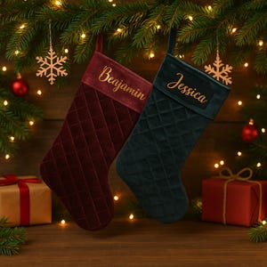 Puede incluir: Dos calcetines de Navidad, uno burdeos y otro verde oscuro, cuelgan sobre un fondo festivo. El calcetín burdeos está bordado con "Benjamin" en dorado, mientras que el calcetín verde dice "Jessica". Ambos calcetines tienen un patrón acolchado.