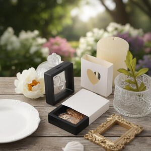 K&ouml;nnte beinhalten: Eine Sammlung von Schmuck-Pr&auml;sentationsboxen, eine Kerze und dekorative Gegenst&auml;nde auf einer Holzoberfl&auml;che. Die Pr&auml;sentationsboxen sind schwarz und wei&szlig; und zeigen Ringe und Halsketten. Ein goldfarbener, verzierter Rahmen und eine klare Glasvase sind ebenfalls vorhanden.