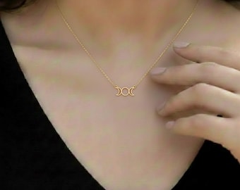 May include: A gold-colored necklace featuring a triple moon pendant. The delicate chain is worn around the neck, with the pendant resting near the collarbone. The necklace is a simple, elegant piece of jewelry.