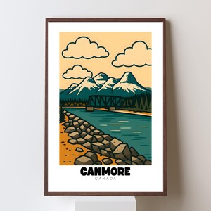 May include: A framed art print featuring a stylized landscape of Canmore, Canada. The artwork depicts mountains, a river, a bridge, and clouds against a yellow sky. The word "CANMORE" and "CANADA" are printed at the bottom in black.