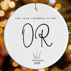 May include: A round white ceramic ornament featuring the black text THE YEAR I WORKED IN THE OR, with the letters OR in a large script font. Below the text are small black medical instrument icons, the name THOMAS, and the year 2026.