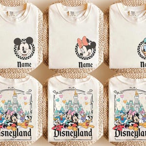 May include: Cream-coloured t-shirts featuring Disney character graphics. Designs include Mickey Mouse, Minnie Mouse, and Donald Duck, each within a chequered circle, and a Disneyland graphic. The word "Name" appears below the character graphics, and "Disneyland 1955" is printed on the bottom.