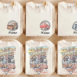 May include: Cream-colored t-shirts with various Cars movie graphics. Designs include Mater, a red fire truck, and a black and white police car, each within a checkered circle. The bottom shirts feature a larger design with multiple characters and the text "Radiator Springs".