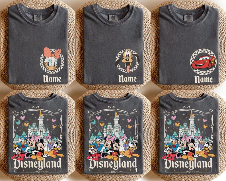 May include: Six grey t-shirts featuring Disney character designs. Three shirts have character portraits with the word "Name" below. The other three shirts feature a Disneyland graphic with the text "Disneyland 1955".