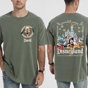 May include: Moss green t-shirt with Pluto's face and the name "David". The back of the shirt has a Disneyland graphic with Mickey, Minnie, Donald, Daisy, and Goofy. The text "Disneyland 1955" is also visible.