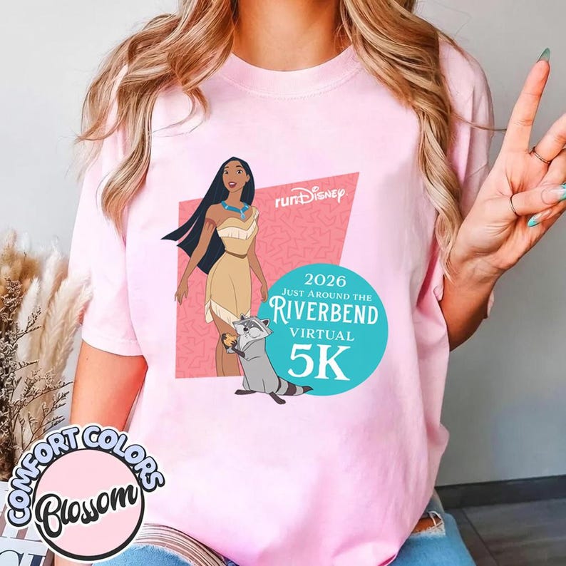 May include: Pink t-shirt featuring a graphic of Pocahontas, a raccoon, and text that reads "Run Disney" and "2026 Just Around the Riverbend Virtual 5K." The shirt also has the "Comfort Colors Blossom" logo.
