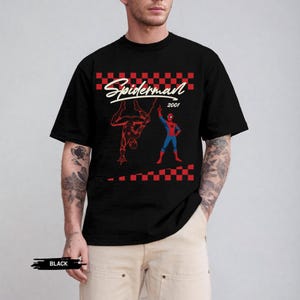 May include: Black t-shirt featuring a Spider-Man graphic. The design includes the word "Spiderman" in white script, the year "2001", and illustrations of Spider-Man in red and blue. A red and black checkered pattern frames the top and bottom of the design.