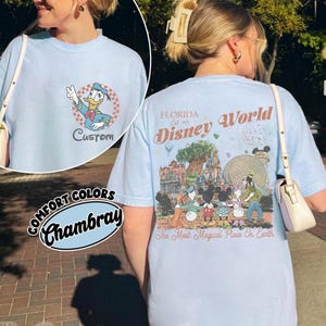 Op de afbeelding: Lichtblauw Comfort Colors Chambray T-shirt met een Donald Duck-afbeelding en het woord "Custom" op de voorkant. De achterkant heeft een Disney World-afbeelding met de tekst "Florida Est. 1971 Disney World" en "The Most Magical Place On Earth."
