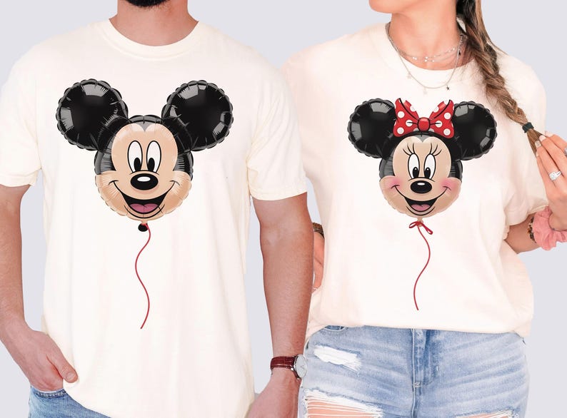 May include: Off-white t-shirts featuring cartoon balloon designs of Mickey and Minnie Mouse. Mickey has a black head with a smiling face and a red string. Minnie has a red bow and a red string. The shirts are casual and suitable for couples.