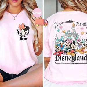 May include: Pale pink t-shirt with a Minnie Mouse graphic and the word "Name" on the front. The back shows a Disneyland design with Mickey Mouse, Donald Duck, and other characters, plus the text "Disneyland 1955."