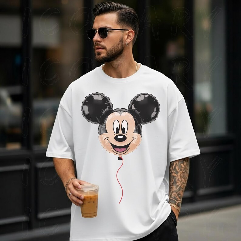 May include: White t-shirt featuring a Mickey Mouse balloon design. The balloon has black ears, a tan face, and a red string. The shirt is a casual style, perfect for everyday wear.