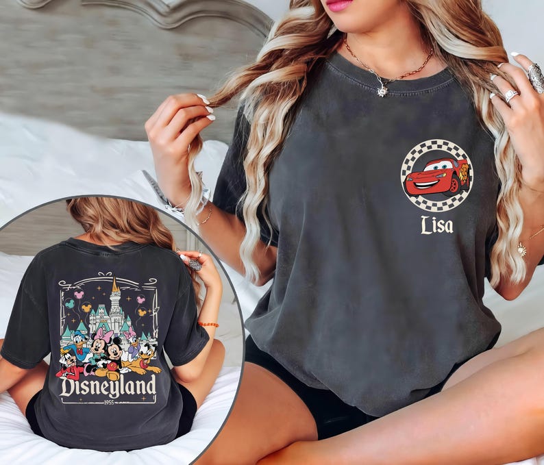 May include: Dark grey t-shirt with a red cartoon race car in a chequered circle, and the name "Lisa" below. The back of the shirt features a Disneyland graphic with cartoon characters and the text "Disneyland 1955".