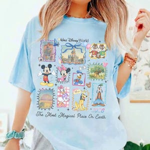 Puede incluir: Camiseta azul claro con un dise&ntilde;o de Disney. El dise&ntilde;o presenta personajes como Mickey y Minnie Mouse, as&iacute; como el texto "Walt Disney World" y "The Most Magical Place On Earth + 2026". El dise&ntilde;o est&aacute; dispuesto en un collage.