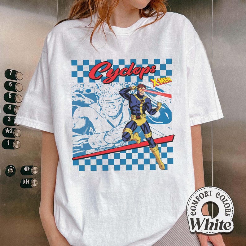 May include: White t-shirt featuring a graphic of the X-Men character Cyclops. The design includes a blue and red checkered pattern, the character's name in red, and a comic book style illustration of Cyclops in action.