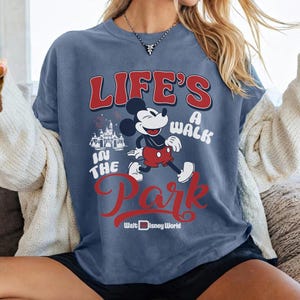 Pu&ograve; includere: T-shirt blu con grafica di Topolino e la scritta "Life's a Walk in the Park" in rosso e bianco. La maglietta include anche il logo Walt Disney World e una grafica del castello.