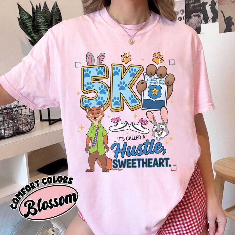May include: Pale pink t-shirt with a cartoon graphic of a fox and bunny, the text "5K", and the words "...IT'S CALLED A HUSTLE, SWEETHEART." The shirt also has the words "COMFORT COLORS" and "Blossom" in a circular design.