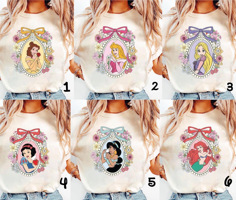 May include: Cream-colored t-shirts featuring six different princess designs. Each design is framed by a floral oval and a ribbon. The princesses include Belle, Aurora, Rapunzel, Snow White, Jasmine, and Ariel.