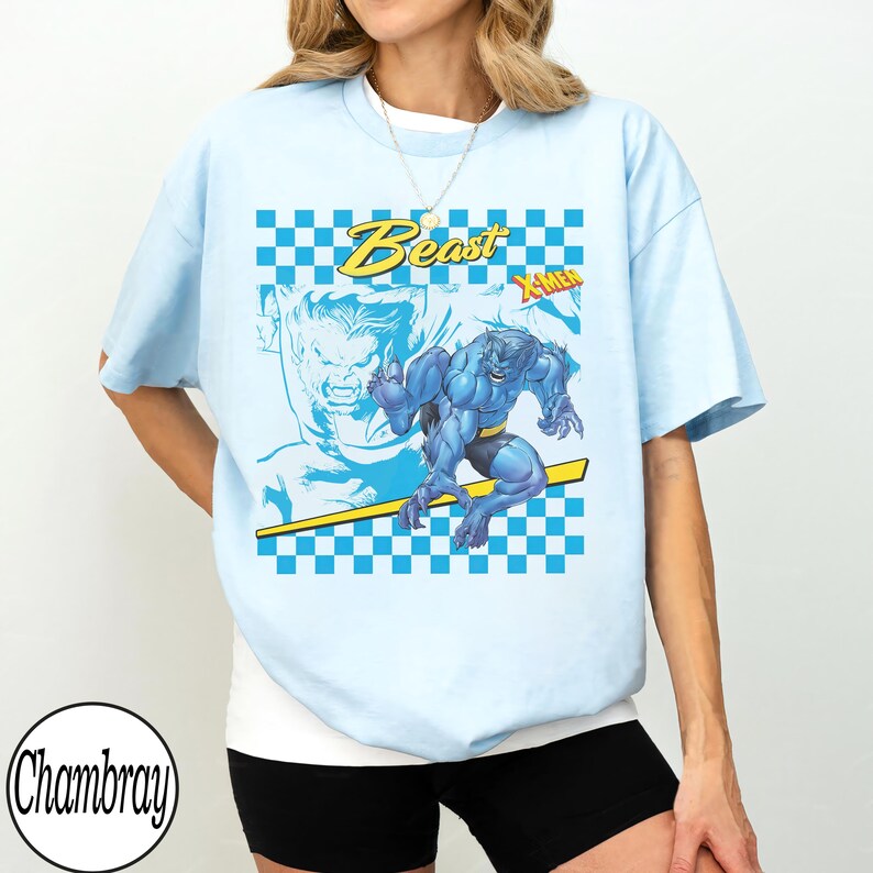 May include: Light blue t-shirt featuring a graphic of the X-Men character Beast. The design includes the word "Beast" in yellow, a blue and white checkered pattern, and the X-Men logo. The shirt is a casual style.