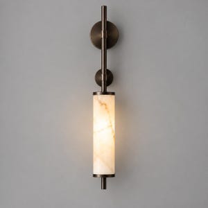Puede incluir: Un aplique de pared con una varilla vertical de metal bronce oscuro y dos placas de montaje circulares. Una pantalla cilíndrica de piedra blanca translúcida con vetas naturales se ilumina desde el interior, emitiendo un brillo cálido.
