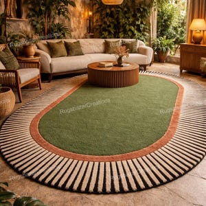 Op de afbeelding: Een ovaal tapijt met een groen midden, een roestkleurige rand en een gestreepte zwart-beige buitenrand. Het tapijt bevindt zich in een woonkamer met een bank, salontafel en hanglampen. De kamer heeft een natuurlijke, aardse uitstraling.