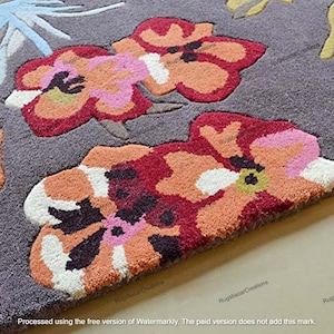 May include: Close-up of a gray rug with large, colorful floral designs. The flowers feature shades of red, orange, pink, and white, with a textured appearance. The rug's background is a solid gray color.