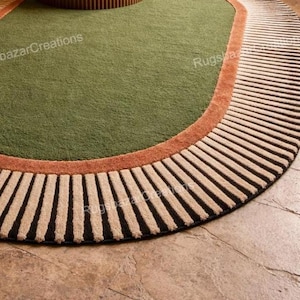 May include: A round area rug with a green center, a rust-colored border, and a striped outer edge. The stripes alternate between black and beige. The rug is placed on a stone floor.