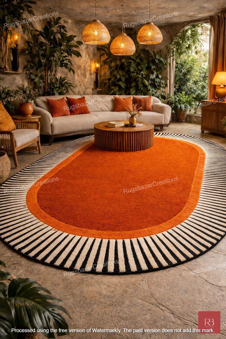 May include: An oval-shaped rug with a vibrant orange center, bordered by a lighter orange band and a black and white striped edge. The rug is placed in a living room setting with a neutral-toned sofa and decorative pillows.