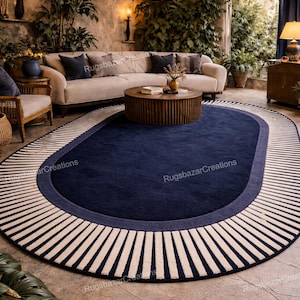 May include: An oval navy blue rug with a striped border. The rug features a dark blue center, a lighter blue border, and a cream and navy striped edge. The rug is in a living room setting.