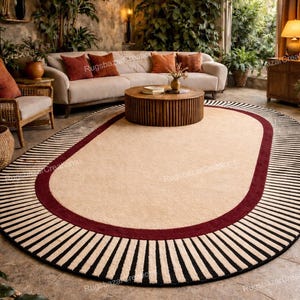 May include: Oval beige rug with a burgundy border and a black and white striped edge. The rug is in a living room setting with a beige sofa, wooden coffee table, and hanging woven lamps. The text "Rugsbazar Creations" is visible.