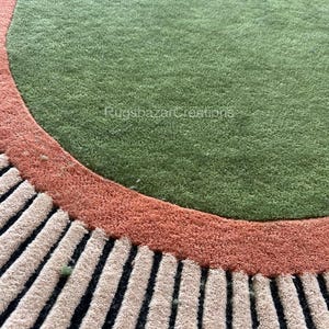 May include: A round rug with a green center, bordered by a rust-colored band and a section of beige and black vertical stripes. The rug has a textured, plush appearance. The text "RugsbazarCreations" is visible.
