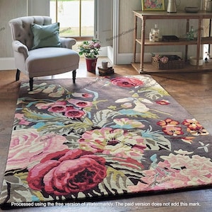 May include: A rectangular area rug with a floral design. The rug features large, colorful flowers in shades of pink, red, and cream against a dark gray background. The rug is placed on a wooden floor.