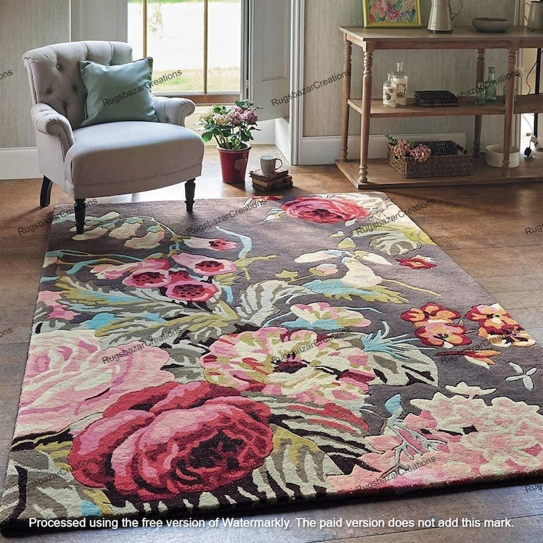 May include: A rectangular area rug with a floral design. The rug features large, colorful flowers in shades of pink, red, and cream against a dark gray background. The rug is placed on a wooden floor.