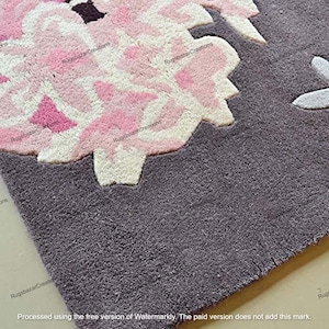 May include: Close-up of a gray rug with a large floral design. The flower is primarily pink and white, with darker pink accents. The rug has a textured appearance, and the floral design is raised.