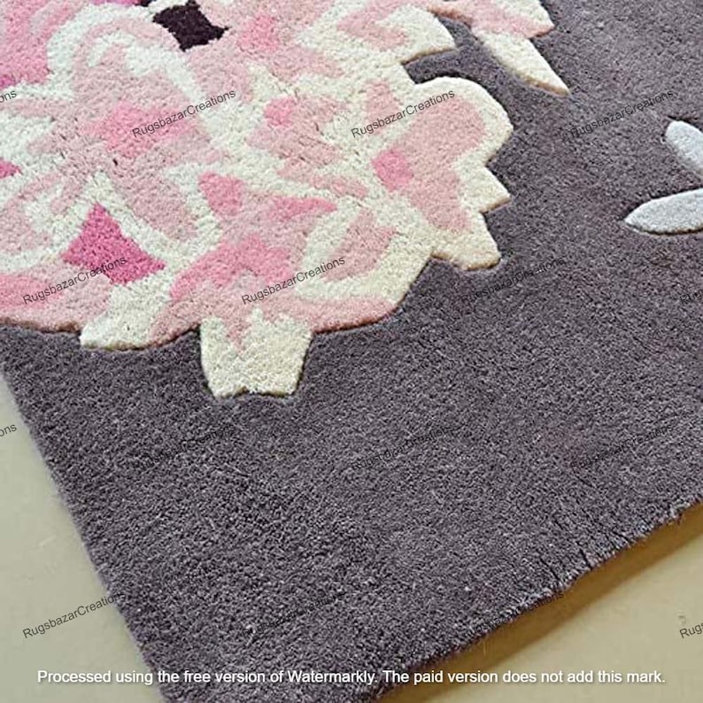 May include: Close-up of a gray rug with a large floral design. The flower is primarily pink and white, with darker pink accents. The rug has a textured appearance, and the floral design is raised.